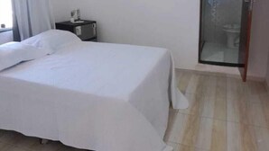 A bedroom with a bed, a nightstand, an air conditioning unit, and a sliding door to a bathroom. - Pousada Sol de Berlinque (Vera Cruz)