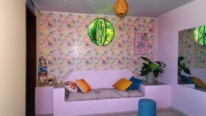 A room with a floral wallpaper, a round mirror, a sofa with cushions, and a potted plant. - Pousada Sol de Berlinque (Vera Cruz)