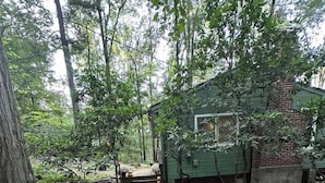 Un sentier en bois mène à un chalet vert, entouré d’arbres et agrémenté d’un parterre de fleurs rouges.