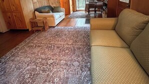 L’intérieur chaleureux d’un chalet avec un canapé, une table à manger et un téléviseur fixé au mur.