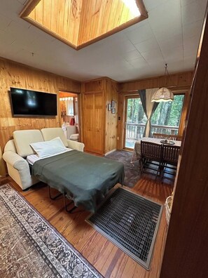A wooden interior with a sofa, a bed, a dining table, and a TV.
