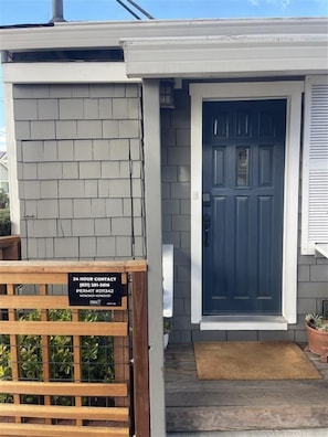 Una casa residencial con revestimiento de tejas grises, una puerta principal azul oscuro y un portón de madera con un letrero de contacto.