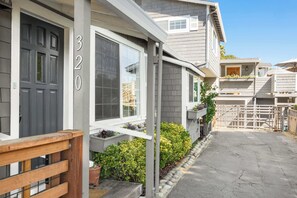 Una propiedad residencial con fachada gris, un porche de madera y un camino de entrada que conduce a una zona vallada.