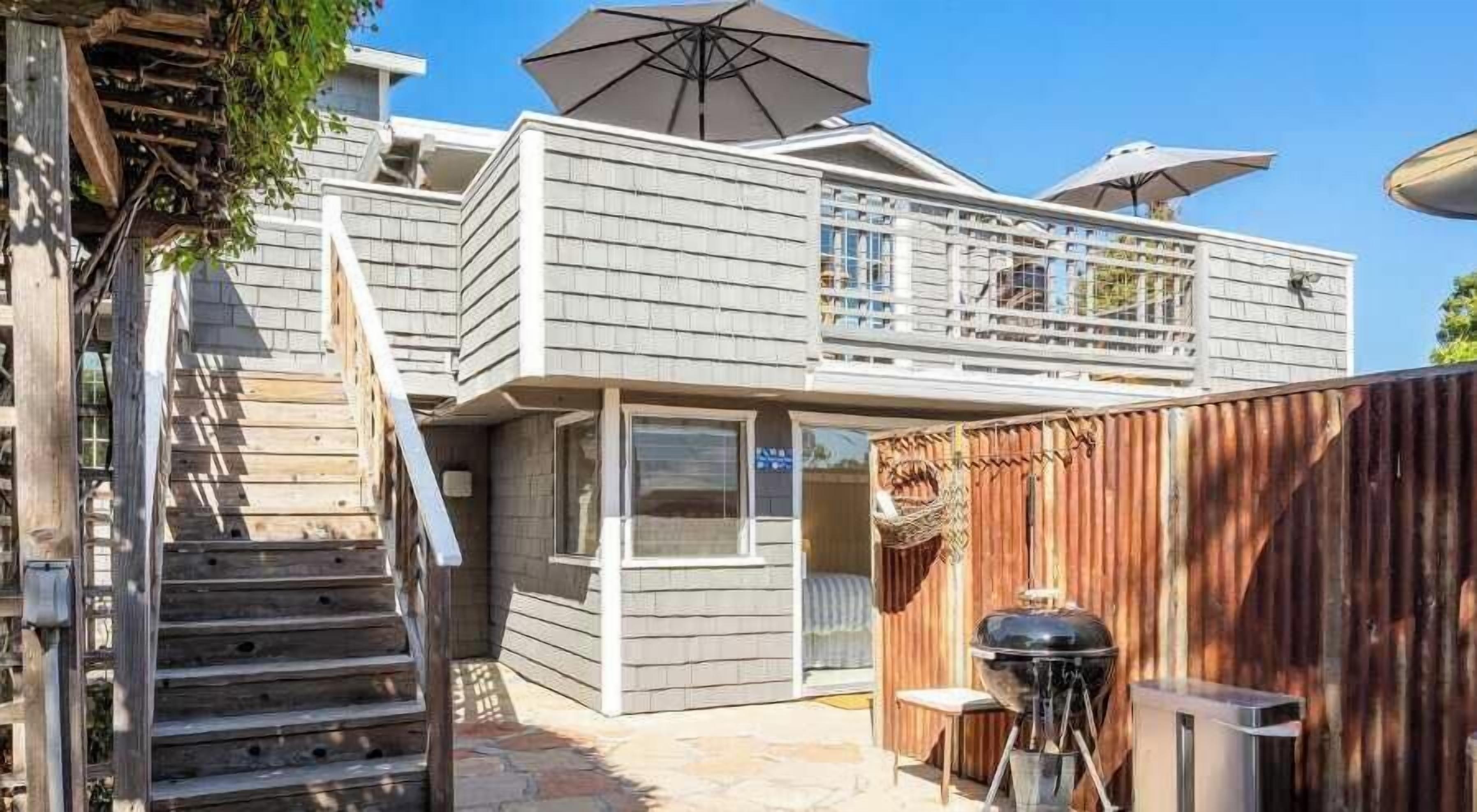 A two-story house with a balcony, a wooden staircase, and a barbecue setup.