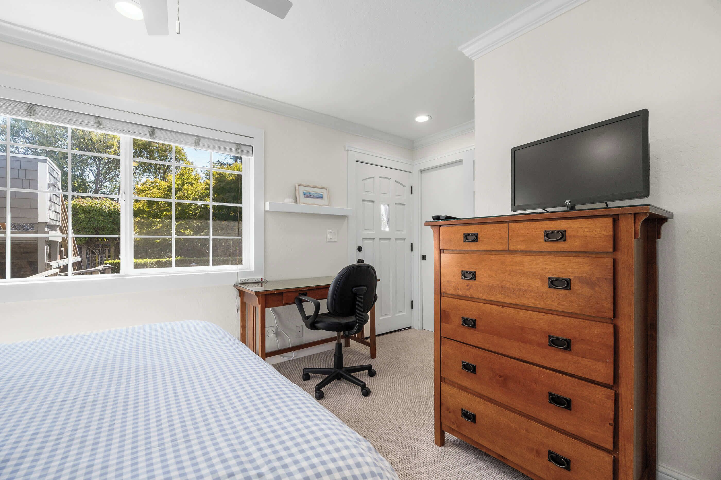 A bedroom with a bed, a desk, a chair, a dresser, and a TV.