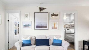 Un salon avec un canapé blanc, des tableaux encadrés accrochés au mur et une porte donnant sur une autre pièce.