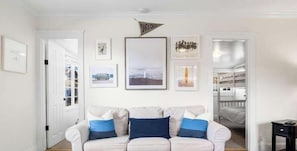 Una sala de estar con un sofá blanco, cuadros en la pared y una puerta que da a otra habitación.