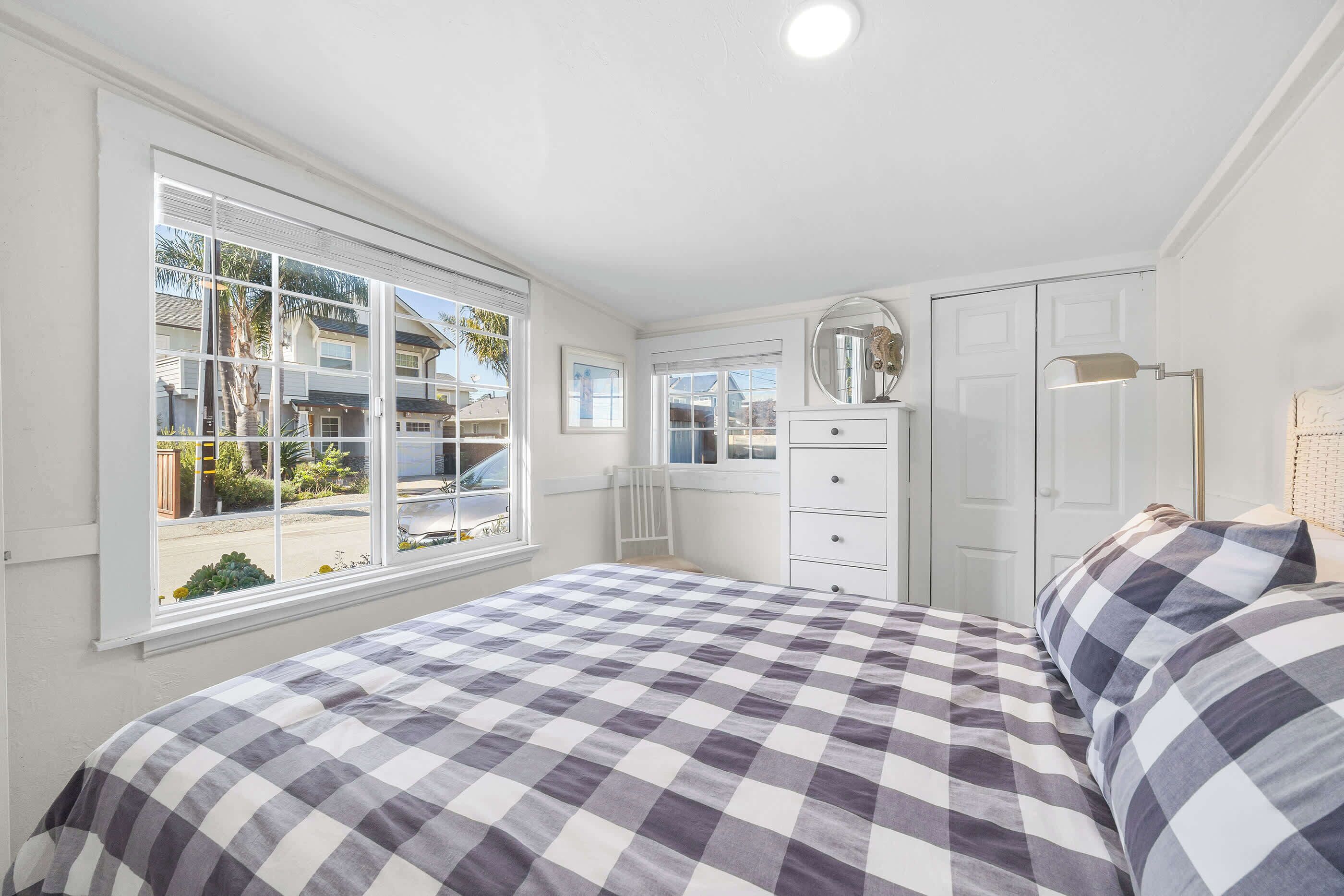 Un dormitorio con edredón a cuadros, cómoda, espejo y ventana con vistas al exterior.
