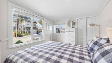 Un dormitorio con edredón a cuadros, cómoda, espejo y ventana con vistas al exterior.