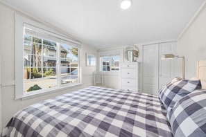 Un dormitorio con edredón a cuadros, cómoda, espejo y ventana con vistas al exterior.