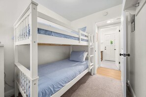 Ein Schlafraum mit Etagenbetten und einer Tür zu einem anderen Zimmer.