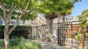 Un espacio exterior compartido con una pérgola de madera, un camino de piedra y abundante vegetación.