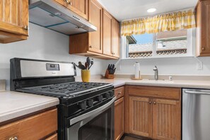 Una cocina con armarios de madera, una estufa de acero inoxidable y un ventanal con cortina amarilla.