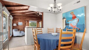 A dining area with a wooden table and chairs, a chandelier, and a painting on the wall. - Twin Lakes Surf Cabin - Sleeps Up To 12 (Santa Cruz)