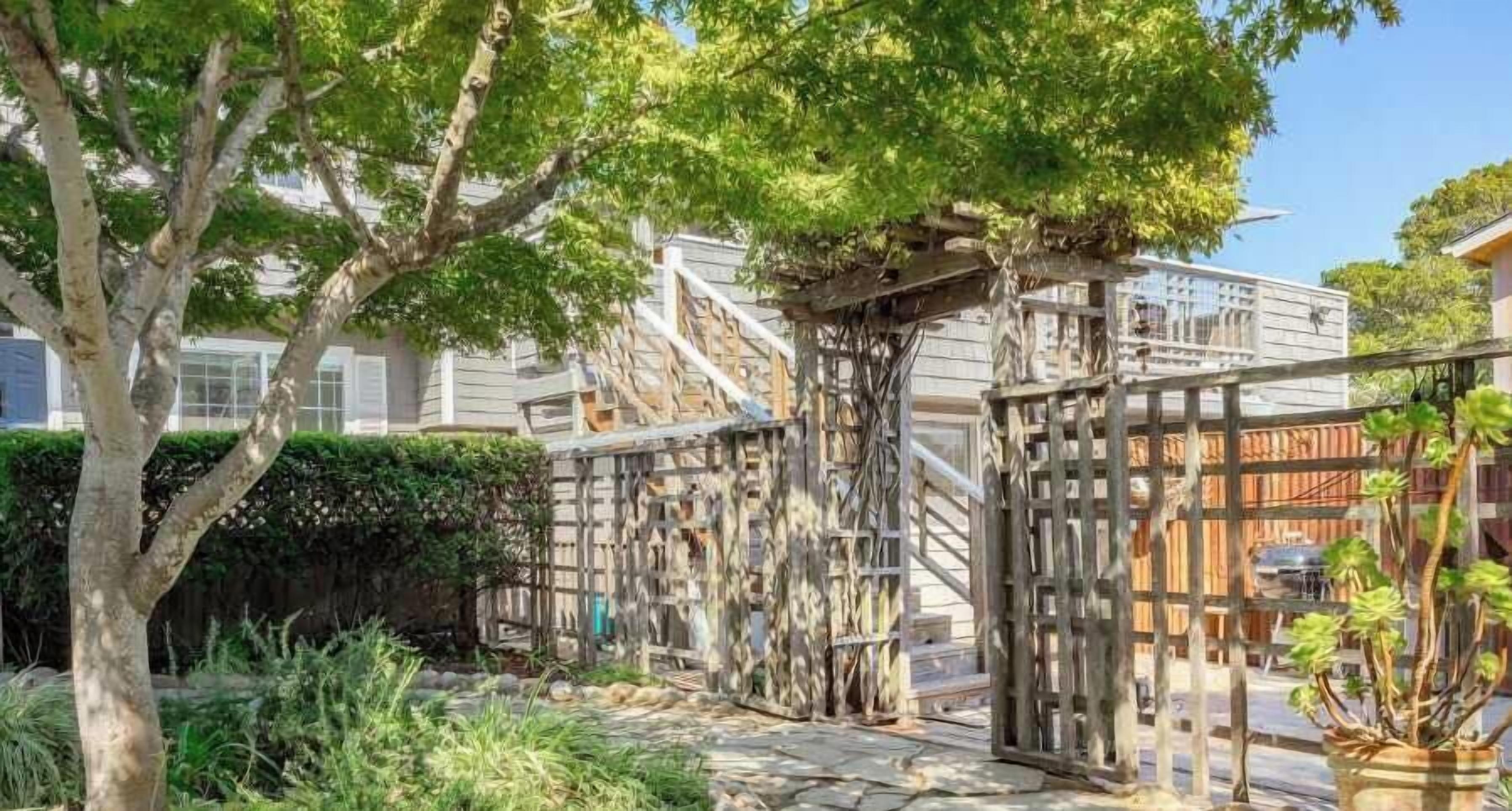 A garden with a wooden pergola, stone pathway, and a variety of plants.
