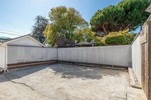 A fenced backyard with a gravel surface, surrounded by a wooden fence and a metal gate.