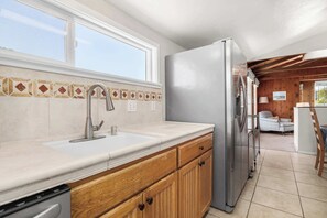 A kitchen with a stainless steel refrigerator, a double sink, wooden cabinets, and a window above the sink.