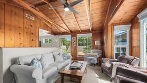 A cozy room with a wooden ceiling, a white sofa with patterned cushions, a brown coffee table, and leather armchairs. - Twin Lakes Surf Cabin - Sleeps Up To 12 (Santa Cruz)