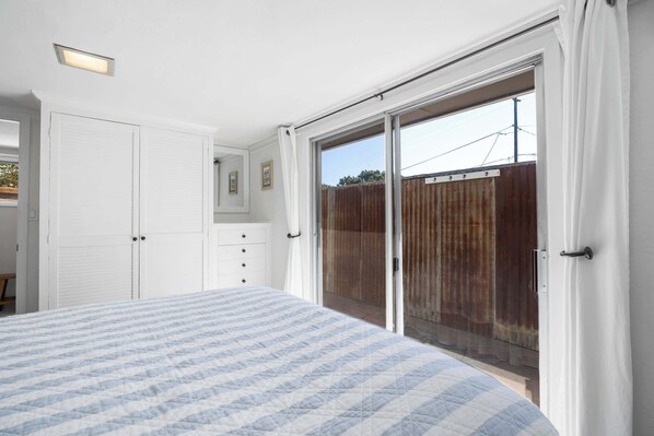 A bedroom with a bed, a wardrobe, a sliding glass door leading to a balcony, and a ceiling light.