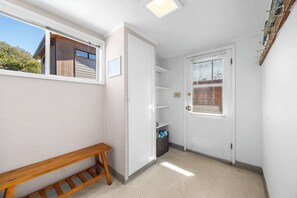 A narrow hallway with a bench, a door with blinds, and a window with a view of the outside.