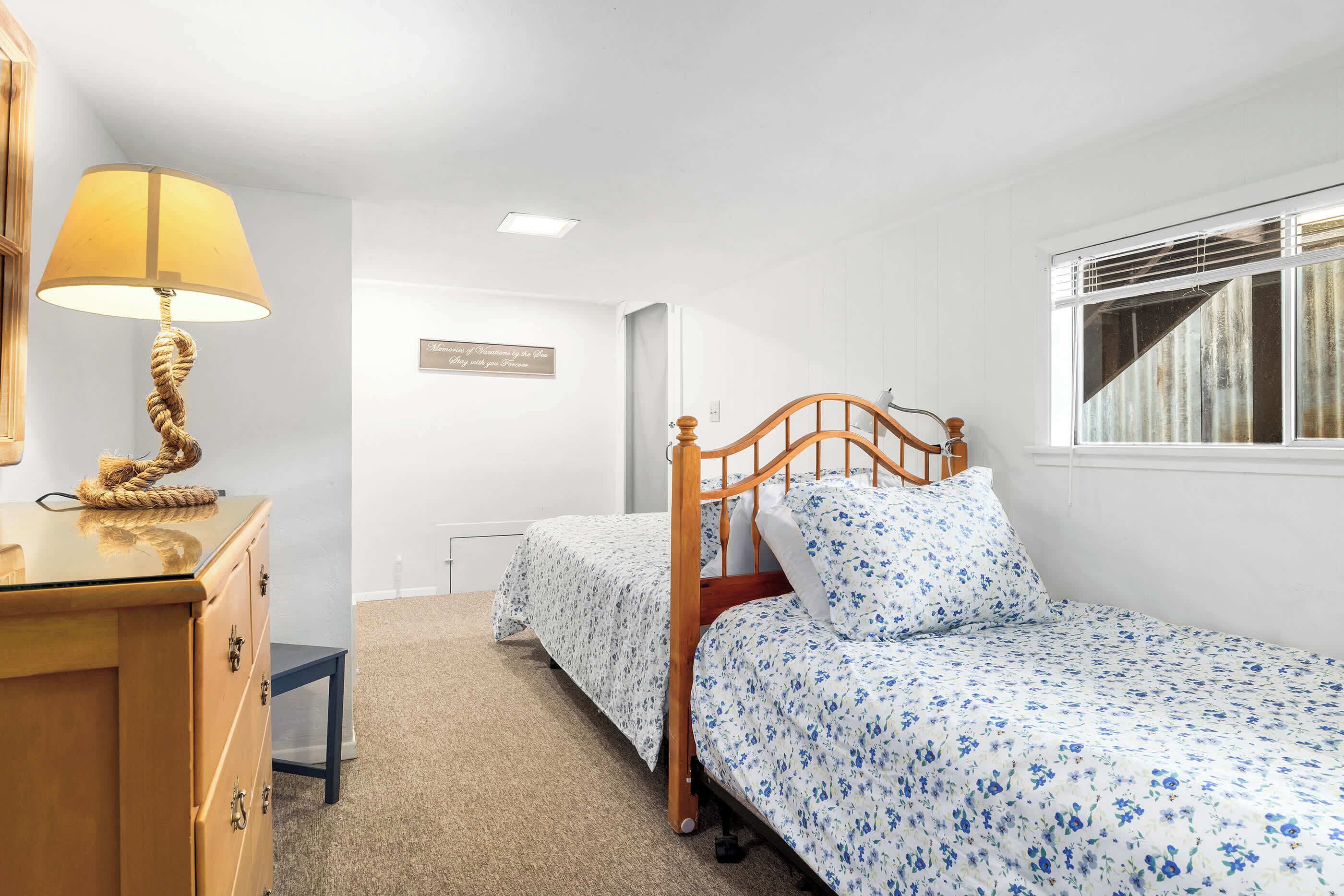 Ein Schlafzimmer mit zwei Betten, einem Holzschrank, einer Lampe und einem Fenster mit Jalousien.