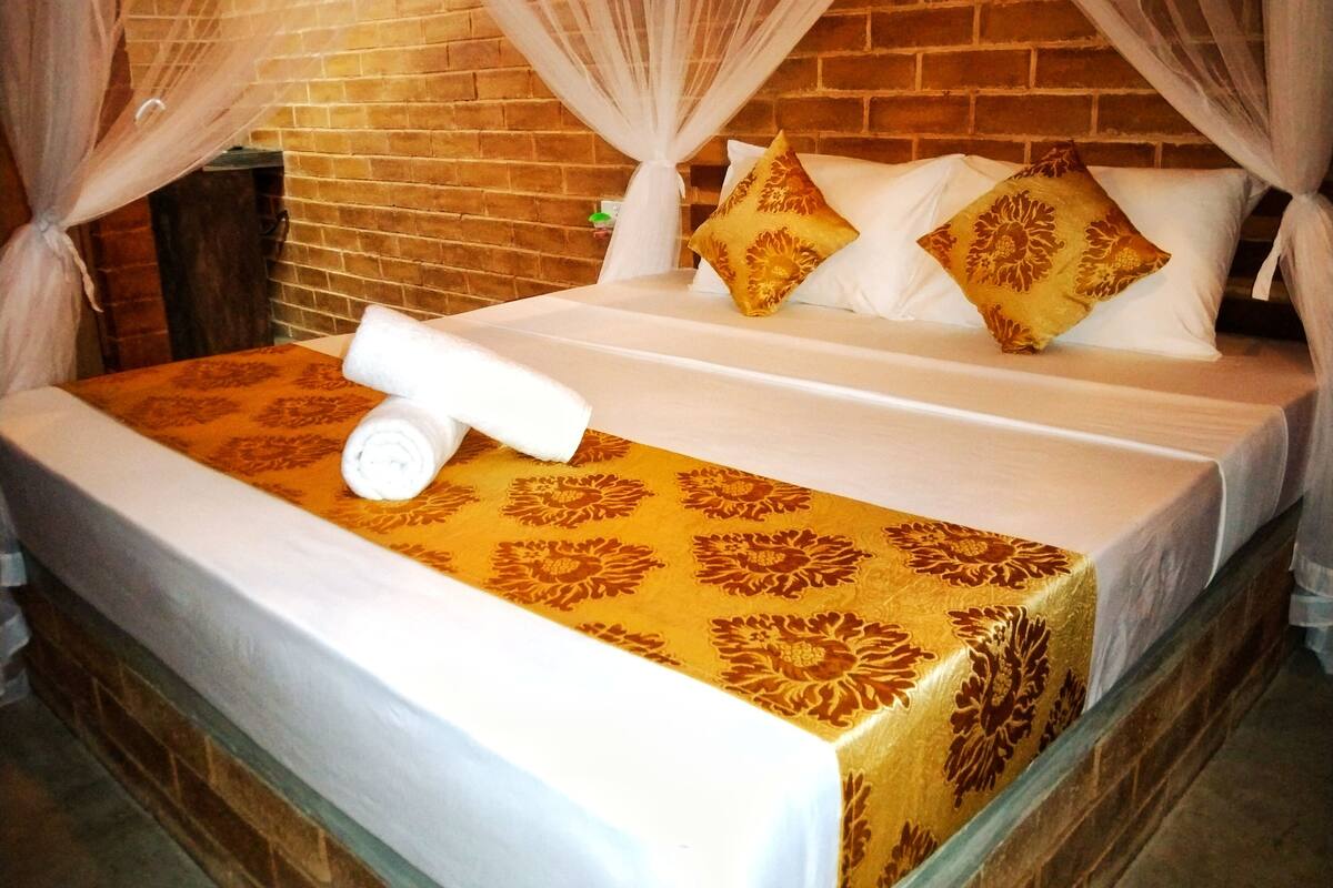 Ein Hotelzimmer mit einer Ziegelwand, einem Himmelbett und einer gemusterten Bettdecke.