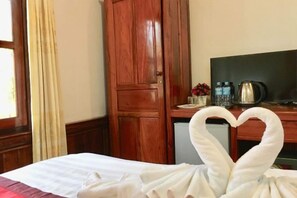 Habitación de hotel con cama, armario de madera, escritorio y televisor, además de una toalla doblada en forma de corazón.