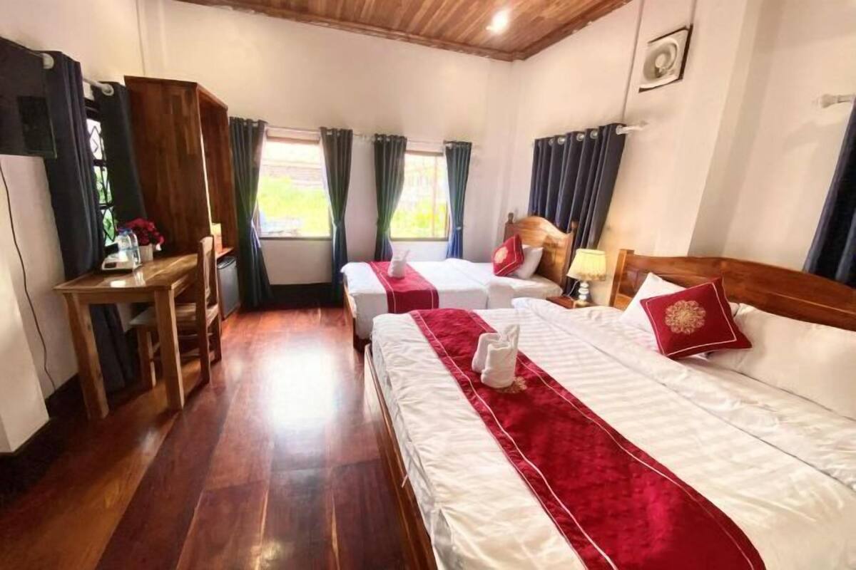 A hotel room with two beds, wooden flooring, a desk, and curtains.