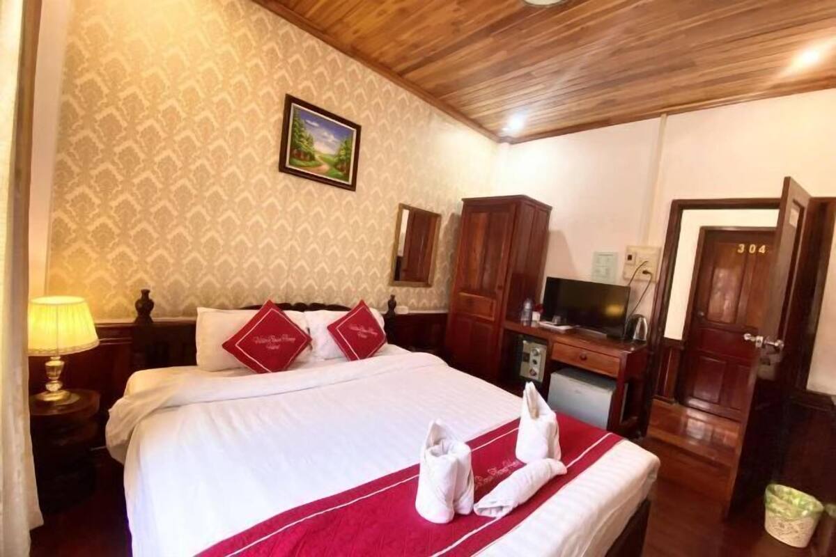 A hotel room with a large bed, a wooden ceiling, a TV, and a desk with a chair.