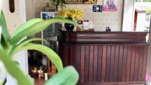 Balcão de recepção com acabamento em madeira, um vaso com flores amarelas e uma parede estampada ao fundo.
