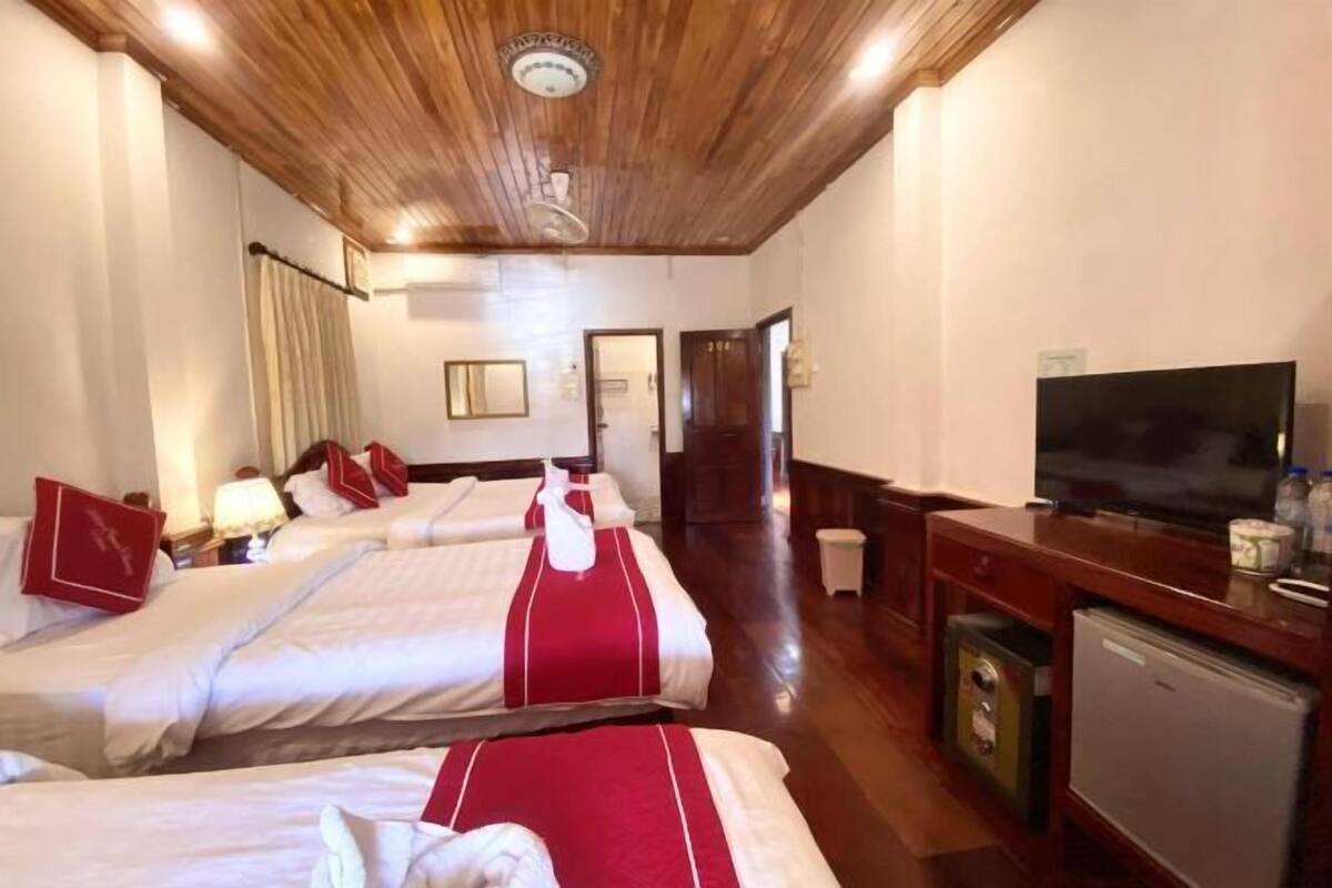 A hotel room with two beds, a television, a small refrigerator, and a wooden ceiling.