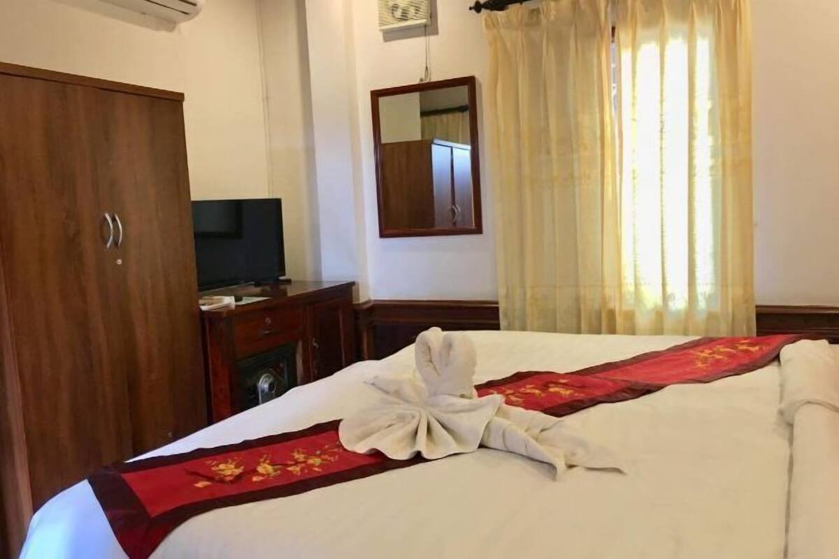 A hotel room with a neatly made bed, a wooden wardrobe, a television on a wooden cabinet, and a mirror on the wall.