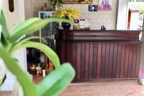 Un mostrador de recepción con detalles de madera, una planta en maceta al frente y un suelo con diseño.