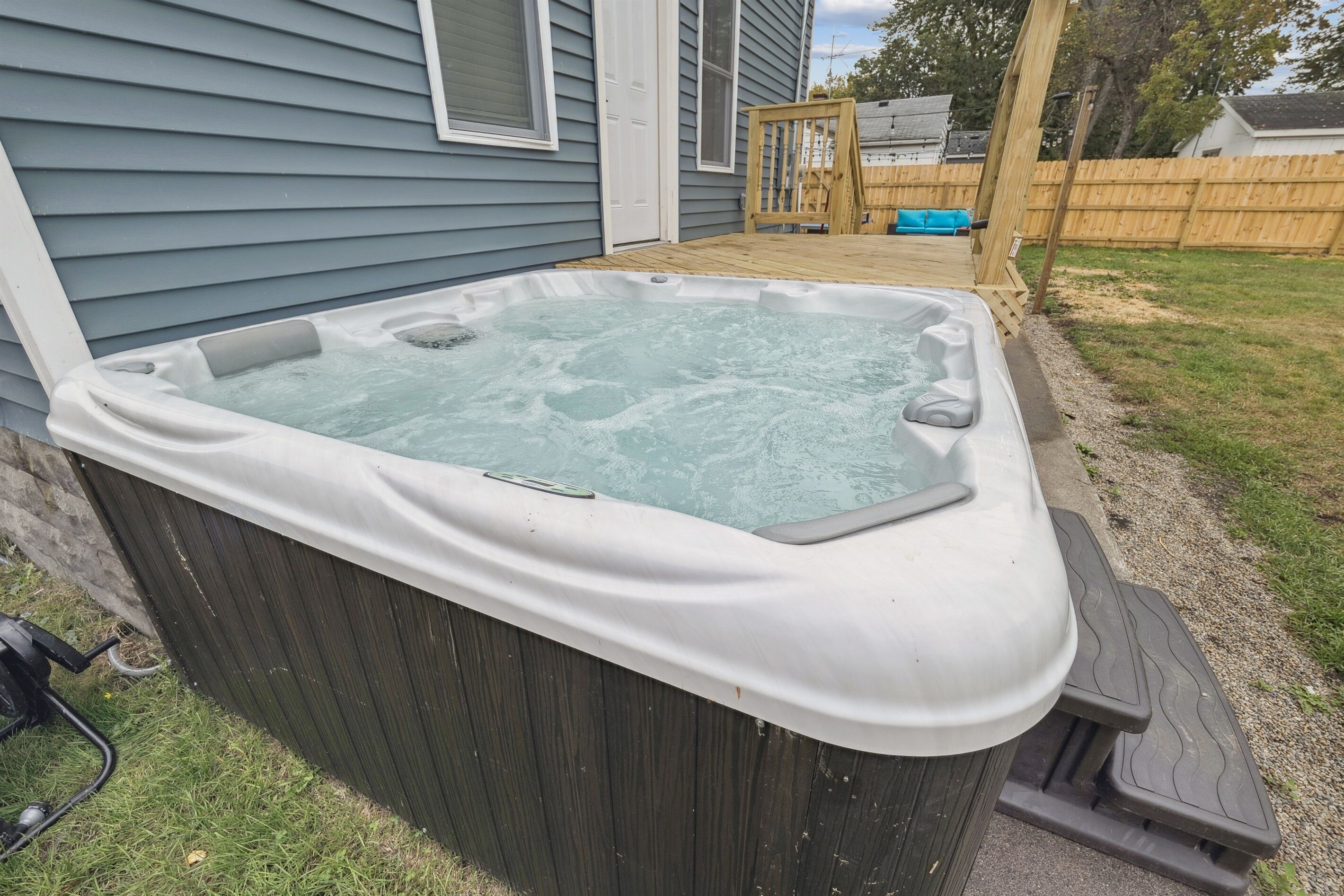 A hot tub adjacent to a house with a wooden deck and a wooden fence in the background.