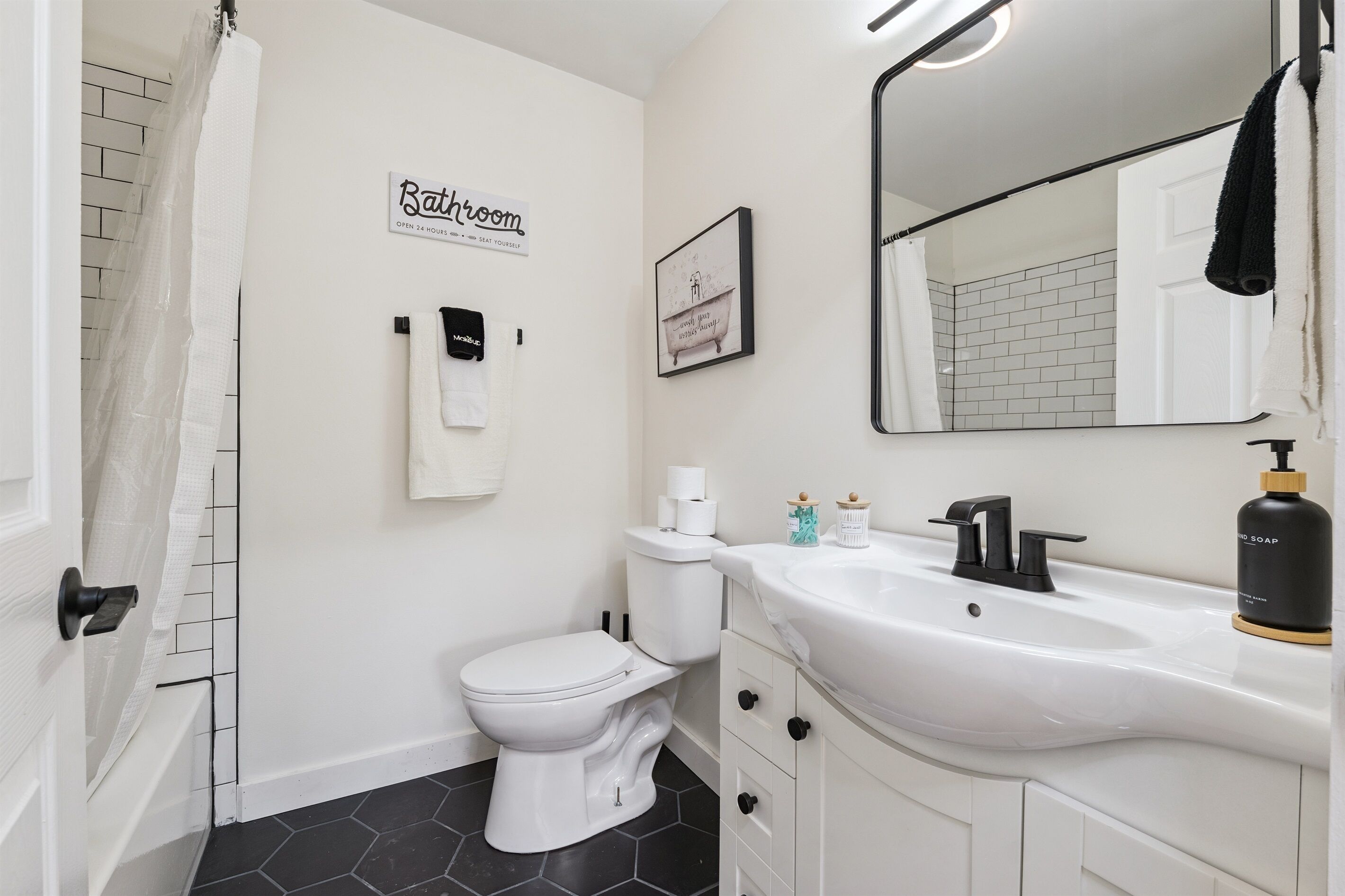 Een badkamer met toilet, wastafel en spiegel. Op de muur hangt een bordje met de tekst 'Badkamer' en een ander bordje met een citaat.