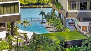 A resort with a pool, lush greenery, and a view of the sea.
