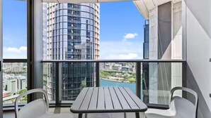A balcony with a table and chairs, offering a view of a tall building and a body of water.
