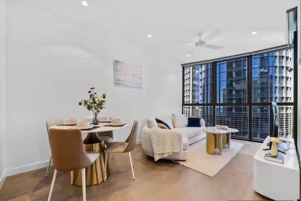 A modern living room with a dining area, large windows, and a ceiling fan.