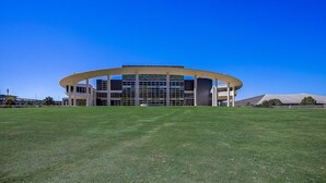 A modern building with a circular central section and a flat roof, surrounded by a well-maintained lawn.