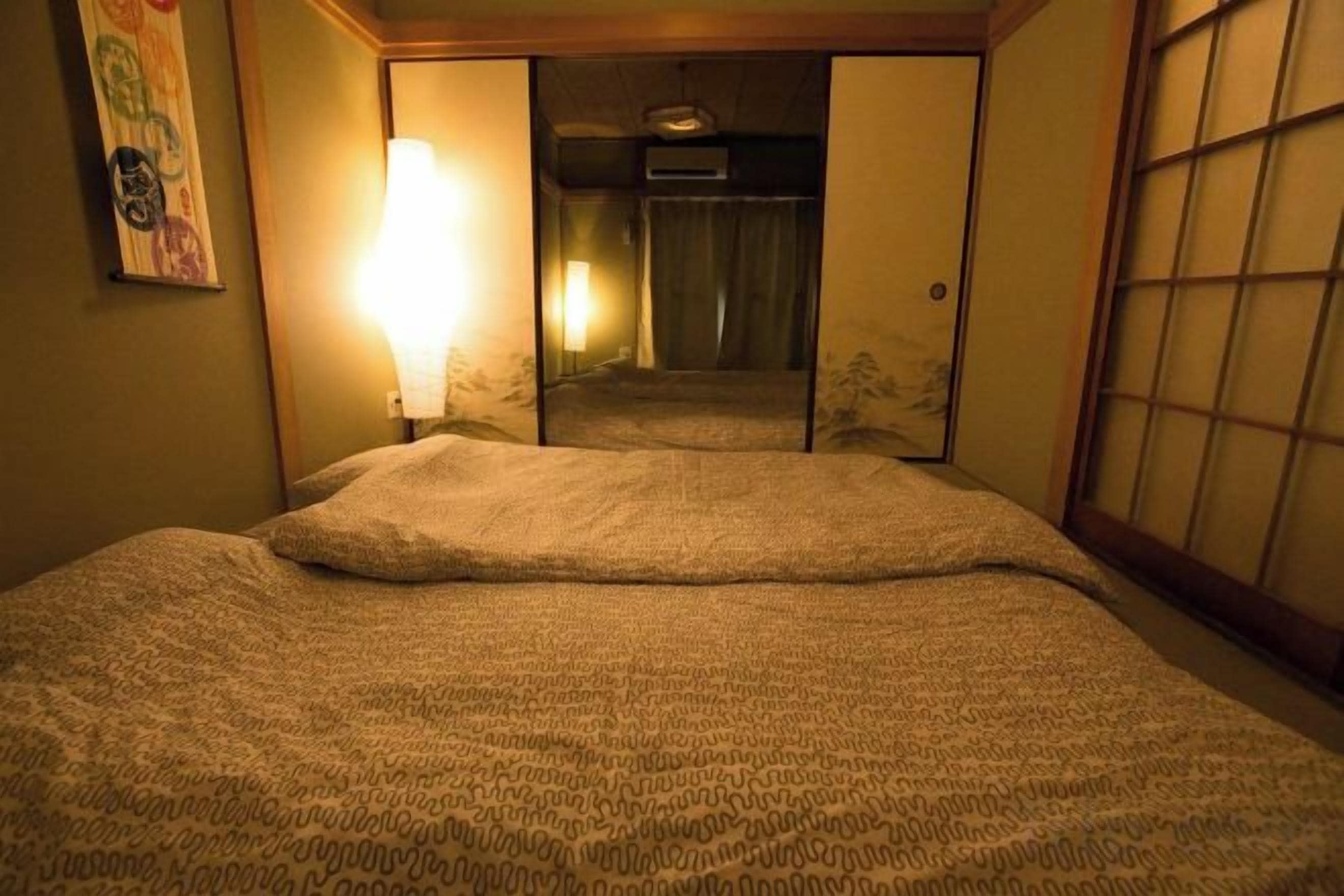 A hotel room with a bed, a wall-mounted lamp, and a sliding door leading to a bathroom.