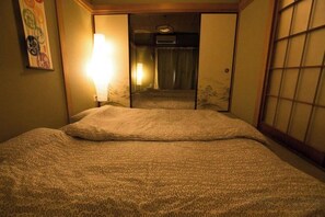 A hotel room with a bed, a wall-mounted lamp, and a sliding door leading to a bathroom. - Nishioi House (Tokyo)
