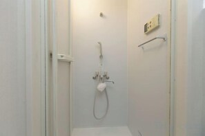 A small, enclosed shower area with a handheld showerhead and a wall-mounted control panel. - Nishioi House (Tokyo)