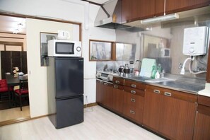 A compact kitchen with a microwave, refrigerator, and wooden cabinets. - Nishioi House (Tokyo)