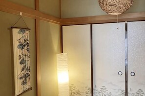 A traditional Japanese room with sliding doors, a hanging floral tapestry, and a hanging lamp. - Nishioi House (Tokyo)