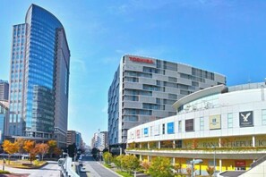 Une rue moderne en milieu urbain, bordée d’immeubles de grande hauteur, dont un gratte-ciel aux façades courbes en verre et un bâtiment orné d’une enseigne Toshiba.