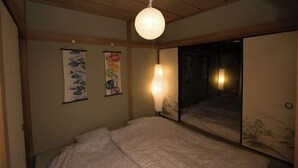 Ein traditioneller japanischer Raum mit Tatami-Böden, einem niedrigen Bett, einer hängenden Papierlaterne und Wandbildern.