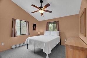 Ein Schlafzimmer mit Bett, Deckenventilator, Fenstern und Nachttisch.