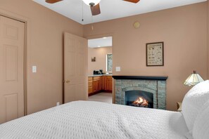 A bedroom with a fireplace, a ceiling fan, and a view into the kitchen.