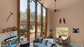 Um quarto amplo com uma grande janela, um sofá, uma mesa de jantar e um ventilador de teto.