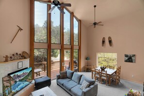 A spacious room with a large window, a sofa, a dining table, and a ceiling fan.